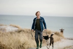 middle aged man walking his dog on the beach