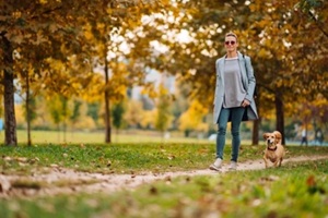 happy woman walking on a park trail with a small brown dog in autumn
